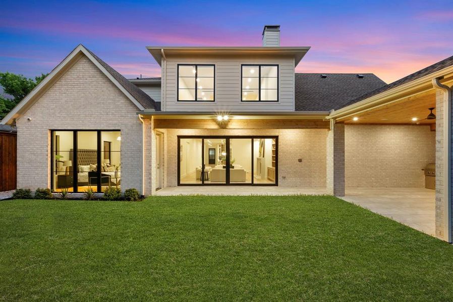 The property features an extensive green lawn, a covered patio area with recessed lighting, and a brick exterior