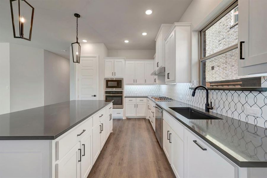 Kitchen with white cabinets, stainless steel appliances, dark wood-type flooring, a kitchen island, and tasteful backsplash