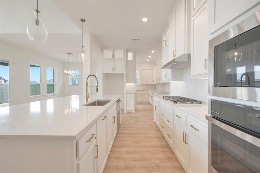 Modern kitchen featuring white cabinetry, light countertops, wood-finish flooring, a kitchen island with an undermount sink, and stainless steel appliances