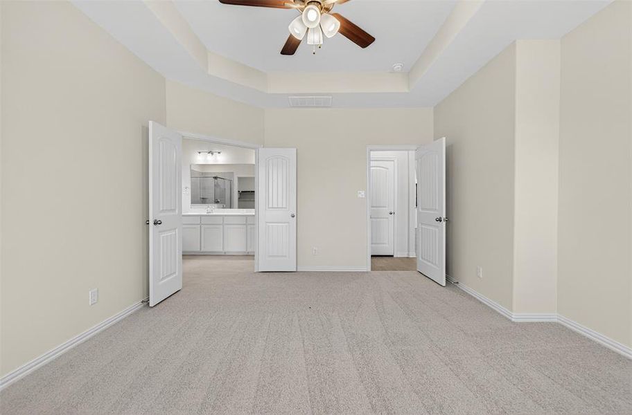 Unfurnished bedroom featuring light colored carpet, a raised ceiling, ceiling fan, ensuite bath, and a high ceiling