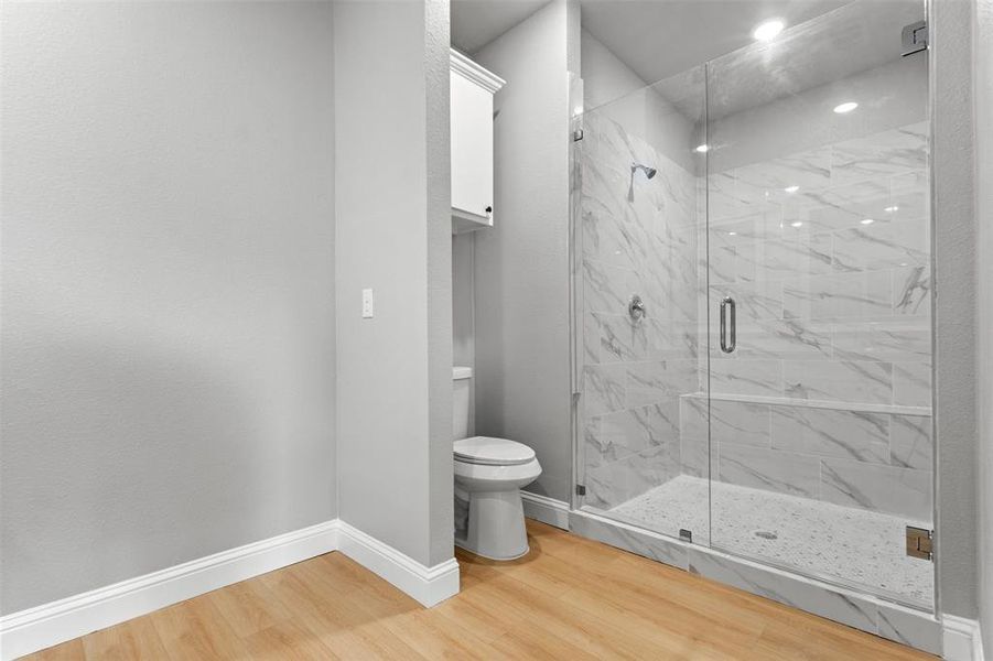 Bathroom with light wood-type flooring and a marble finish shower