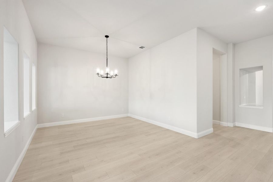 Empty dining room with light wood floors, white walls, and a black chandelier overhead