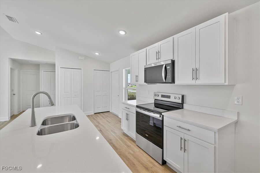 Kitchen featuring appliances with stainless steel finishes, white cabinetry, lofted ceiling, recessed lighting, and light wood finished floors