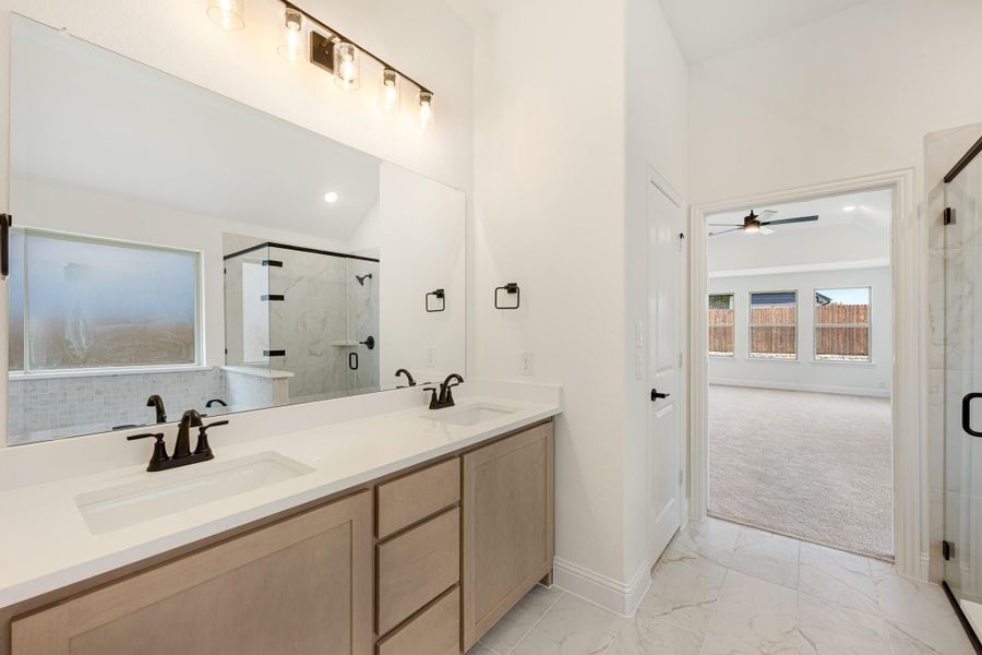 Master bathroom with double vanity, white countertops, glass shower, and marble tile floors