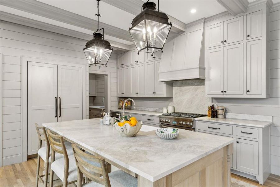 Kitchen featuring a center island with sink, light stone counters, high end range, hanging light fixtures, and wall chimney range hood