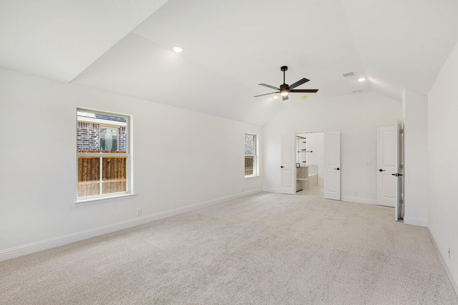 Spacious bedroom with vaulted ceiling, ceiling fan, carpet flooring, and open doors to closet and bathroom.