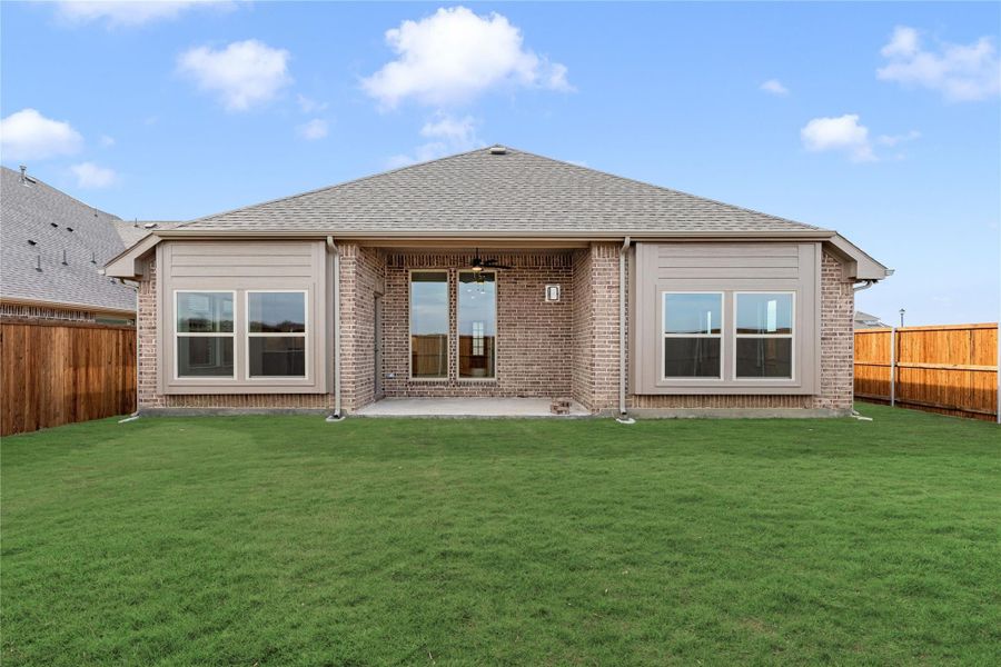 Rear exterior of single-story brick home with covered patio, large windows, and fenced backyard with green lawn Rear exterior of single-story brick home with covered patio, large windows, and fenced backyard with green lawn