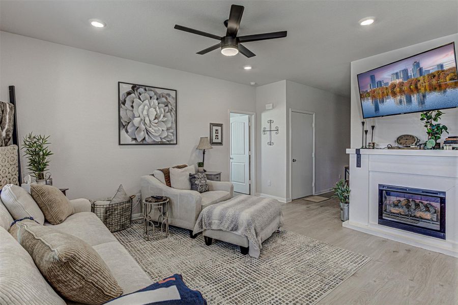 Living area with a ceiling fan, wood finished floors, a glass covered fireplace, and recessed lighting