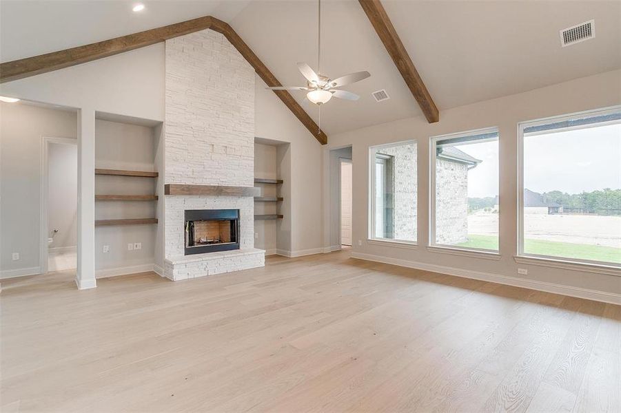 Unfurnished living room featuring ceiling fan, built in shelves, high vaulted ceiling, light wood-type flooring, and a stone fireplace