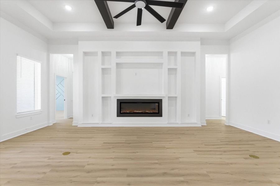 WOW factor. A living room crafted with intention, featuring an ample electric fireplace, custom built-ins, ceiling beams, and additional floor outlets for all your electronics.