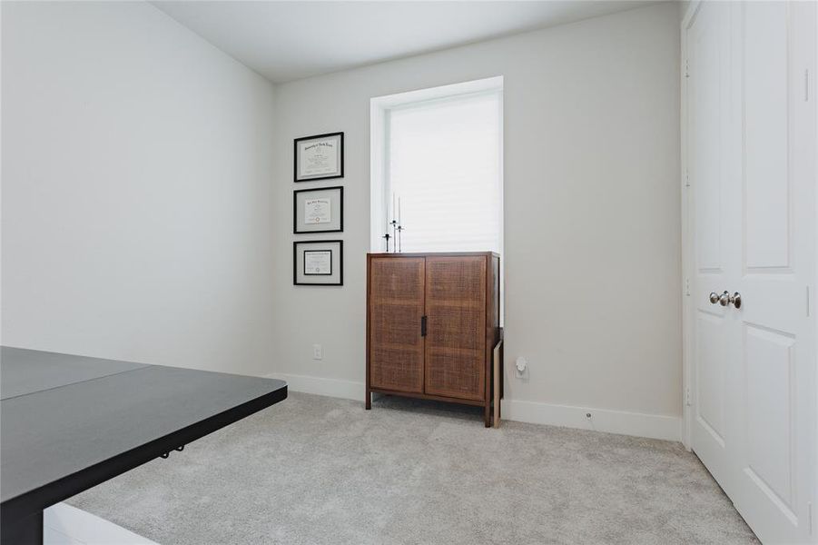 Currently serving as an office is the 2nd bedroom, carpeted interior space featuring light-toned walls, white trim, and a window with blinds
