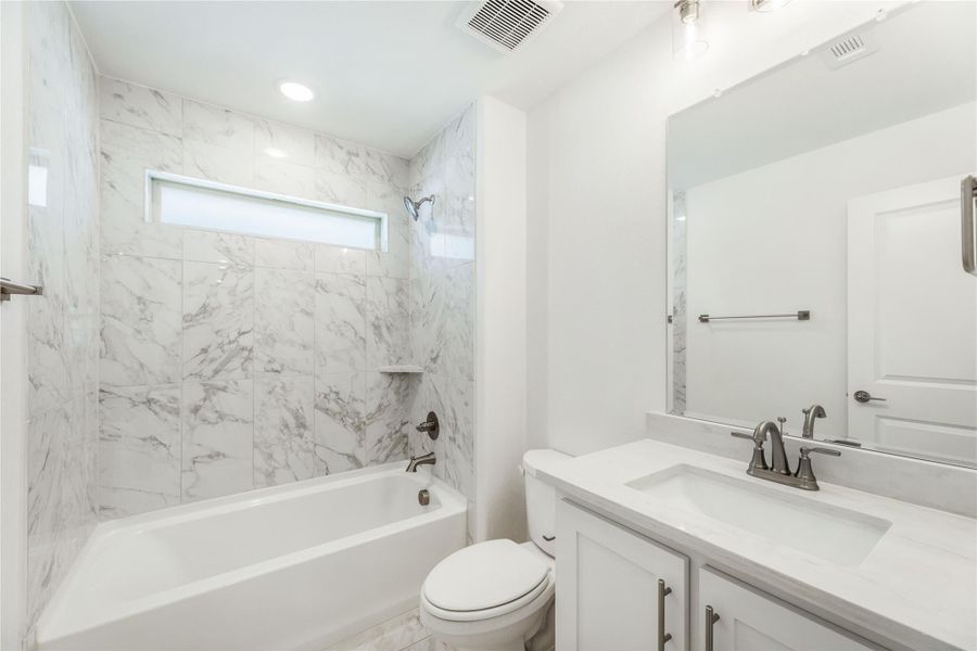Bathroom with marble-tile tub surround, white vanity with quartz countertop, and toilet