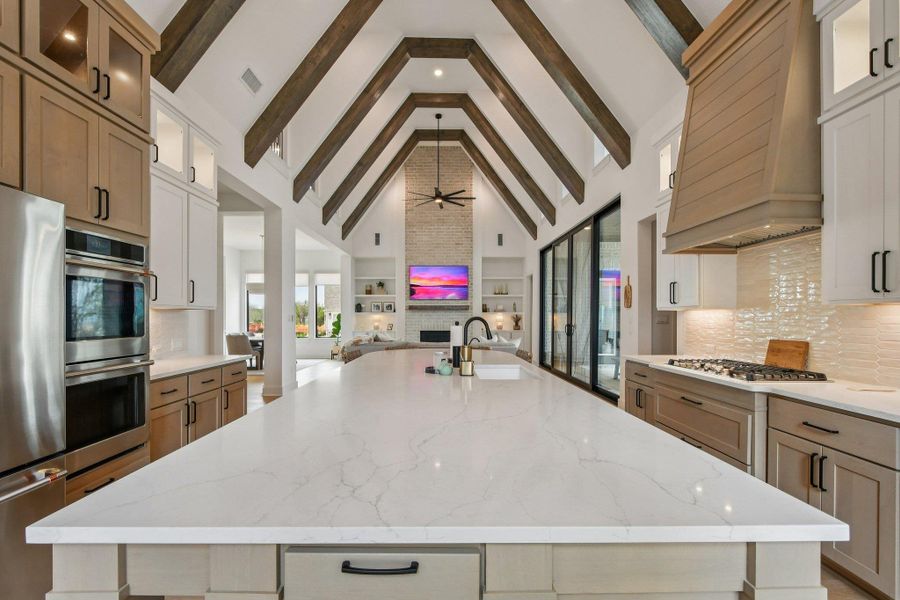 The kitchen features an expansive island with a white countertop, stainless steel appliances, and a gas range with a decorative hood The kitchen features an expansive island with a white countertop, stainless steel appliances, and a gas range with a decorative hood