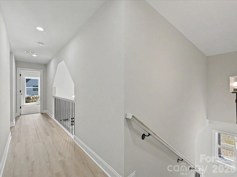 Open upper-level landing overlooks the main living area and provides a bright, airy transition between bedrooms with modern railing details.
