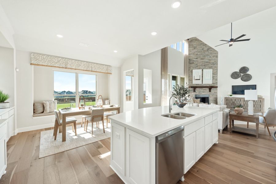 Open-concept kitchen with white island, hardwood floors, and stone fireplace leading to dining area