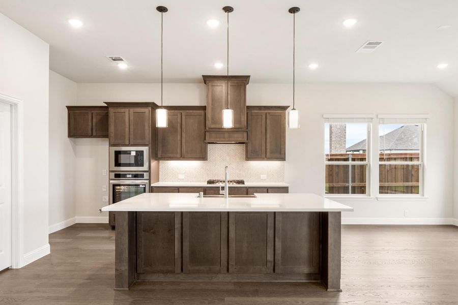 Kitchen with large center island, dark brown cabinets, white countertops, and three pendant lights above the island.
