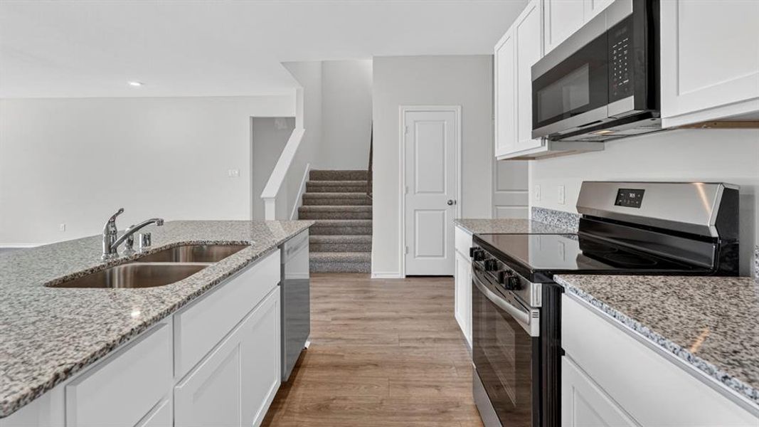 Kitchen featuring granite countertops, white cabinetry, a double basin stainless steel sink, stainless steel appliances, and wood-finish flooring Kitchen featuring granite countertops, white cabinetry, a double basin stainless steel sink, stainless steel appliances, and wood-finish flooring