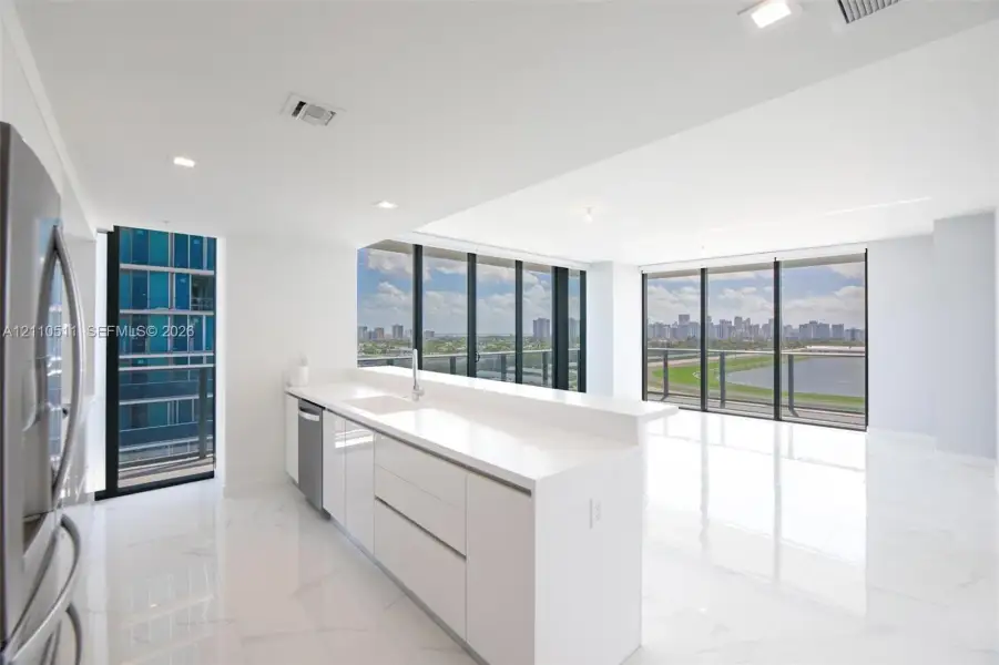 Modern kitchen featuring white flat-panel cabinetry, quartz countertops, a stainless steel dishwasher, stone-finish tile flooring, and floor-to-ceiling windows