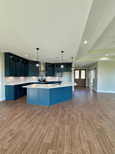 This spacious kitchen features modern dark cabinetry and a large central island with a light countertop. It includes a stylish backsplash, pendant lighting, and wood-look tile flooring, providing a contemporary and inviting space. This spacious kitchen features modern dark cabinetry and a large central island with a light countertop. It includes a stylish backsplash, pendant lighting, and wood-look tile flooring, providing a contemporary and inviting space.