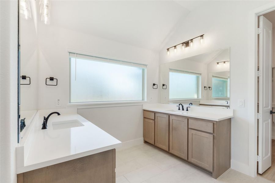Bathroom with dual vanities, wood cabinets, white countertops, and frosted windows with vaulted ceiling