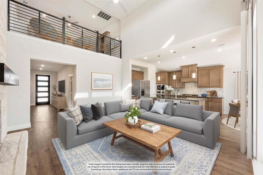 Open-concept living room with two-story ceiling, upper loft railing, and kitchen visible in background Open-concept living room with two-story ceiling, upper loft railing, and kitchen visible in background
