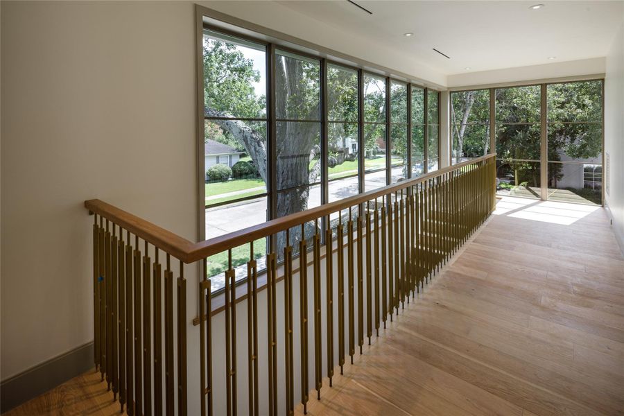 This view is hard to beat. Floor-to-ceiling windows wrap the upstairs landing in mature treetop views, bringing the established neighborhood right into this newly completed home. The brass railing is just the finishing touch.