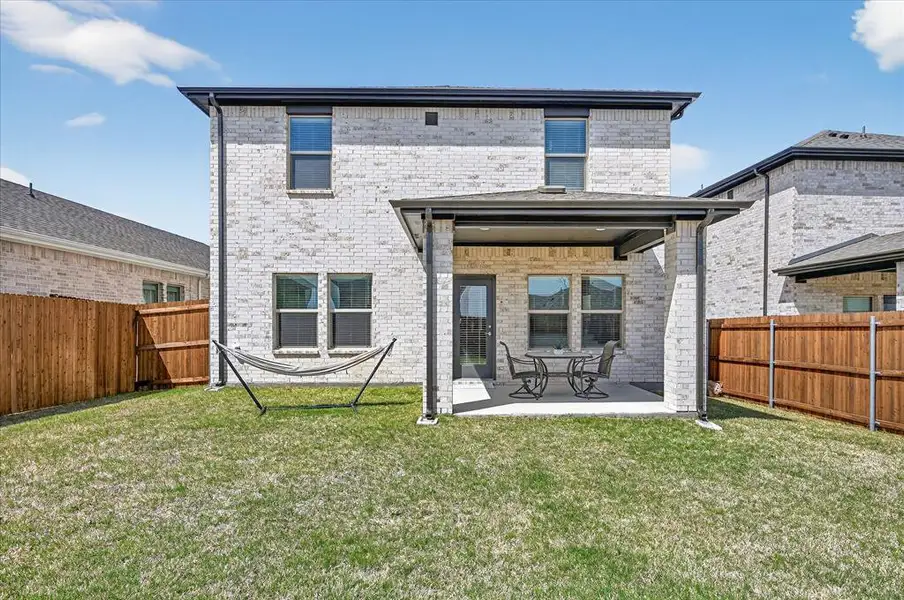 Rear view of property featuring brick siding, a fenced backyard, and a patio area
