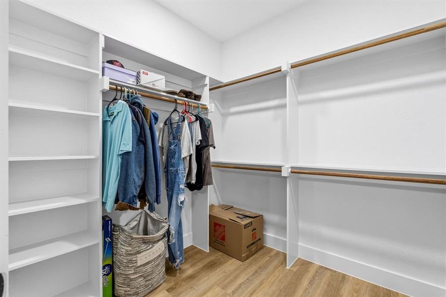 Walk-in closet featuring built-in shelving, multiple hanging rods, and wood-finish flooring