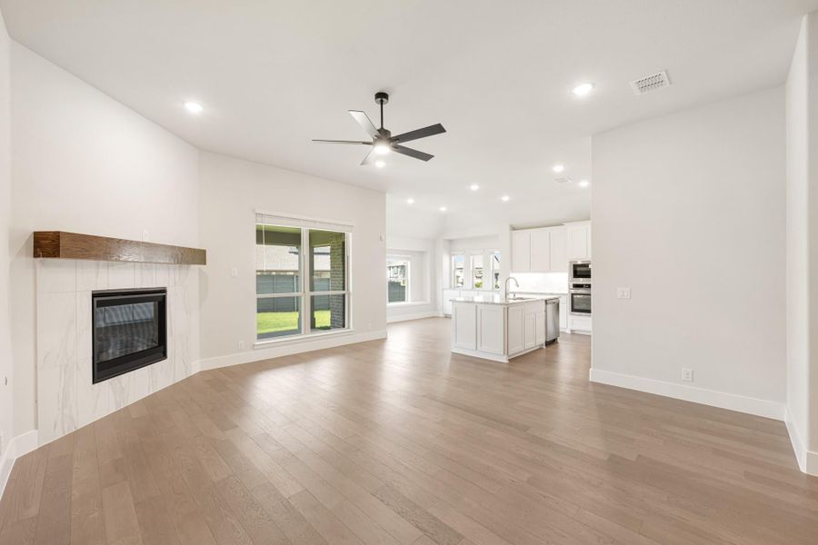 Open living area with hardwood floors, fireplace, and ceiling fan, open to white kitchen with island