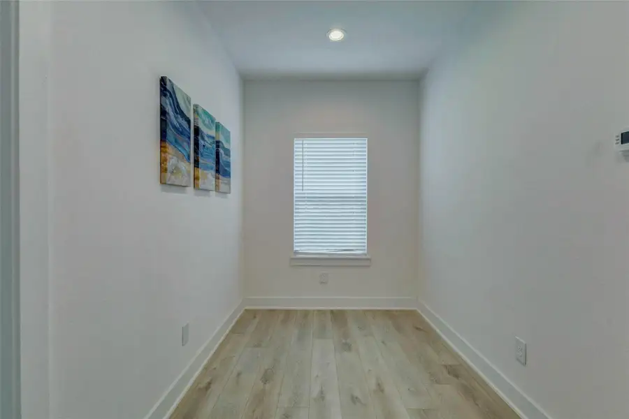 Narrow flex room or office space with wood-look flooring, tall window with blinds, recessed lighting, neutral walls, and a quiet tucked-away layout. This versatile room works well as a home office, study area, workout nook, storage space, or creative retreat.