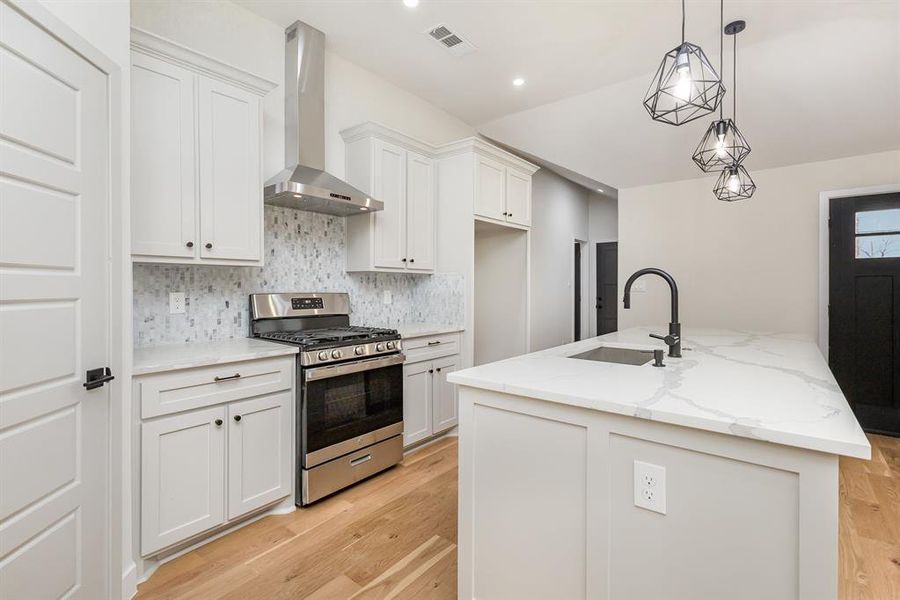 Kitchen with stainless steel range with gas cooktop, a sink, light wood-style floors, wall chimney range hood, and backsplash