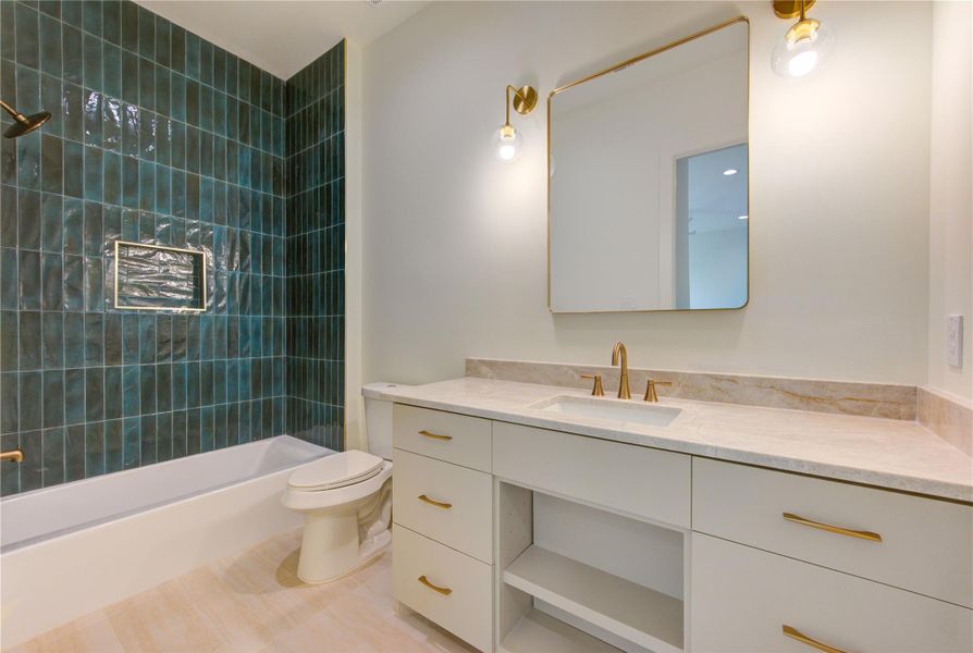 This secondary ensuite bath continues the home's elevated design aesthetic with a striking feature wall of rich emerald-green handcrafted tile, creating a sophisticated designer statement. Quartzite countertops add both beauty and durability, while custom cabinetry with warm brass hardware provides ample storage and a refined, contemporary feel.