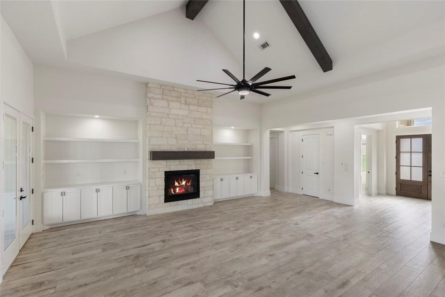 Living room with fire place, built in cabinets and shelves with a stone feature wall and mantel. A large ceiling fan with wood beams to accent. Living room with fire place, built in cabinets and shelves with a stone feature wall and mantel. A large ceiling fan with wood beams to accent.