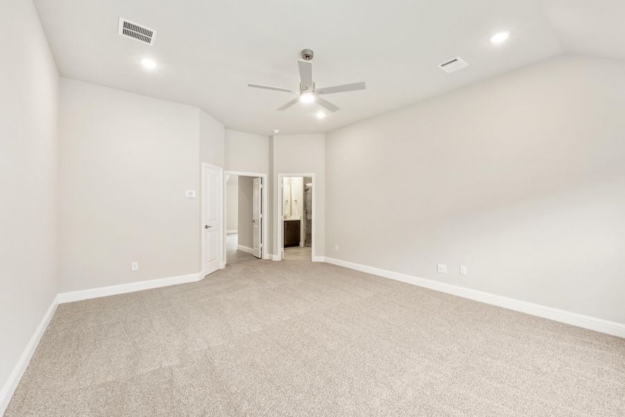 Empty bedroom with carpet flooring, ceiling fan, and open door leading to ensuite bathroom