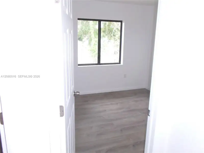 Room featuring wood-finish flooring, white walls, and a window with a dark frame