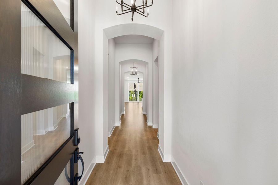 Striking entry hall with arched ceilings, warm wood-look floors, and a modern glass-panel front door.