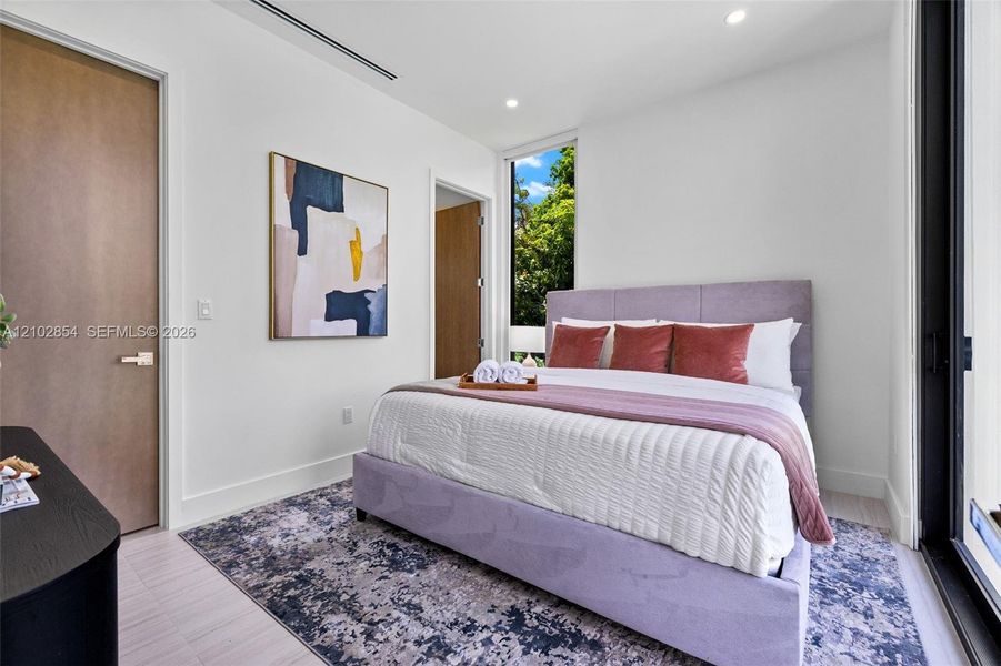 Minimalist bedroom featuring floor-to-ceiling windows, recessed lighting, smooth-finish interior doors, and pale wood-finish flooring