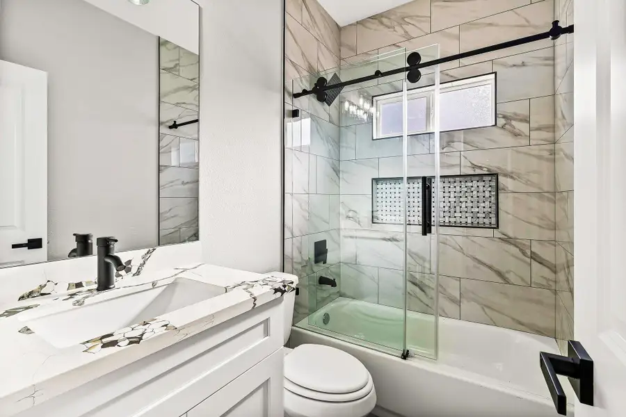 This bathroom features a modern design with a sleek glass shower door, marble-patterned tiles, and a stylish vanity with a unique sink design. Matte black fixtures add a contemporary touch, while the window provides natural light. This bathroom features a modern design with a sleek glass shower door, marble-patterned tiles, and a stylish vanity with a unique sink design. Matte black fixtures add a contemporary touch, while the window provides natural light.