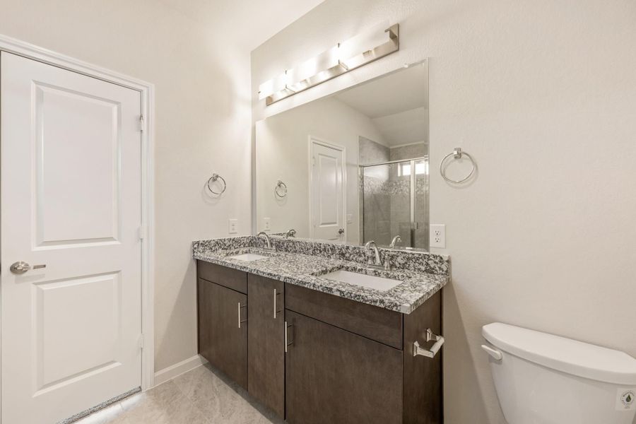 Bathroom with double sink vanity, dark wood cabinets, granite countertop, large mirror, and walk-in shower