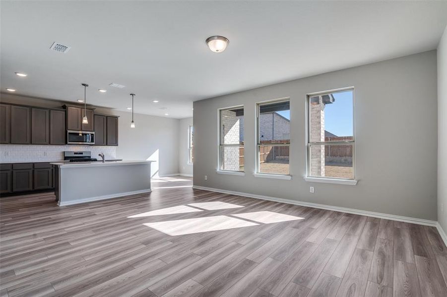 Kitchen with open floor plan, pendant lighting, backsplash, dark brown cabinets, and light wood-style floors Kitchen with open floor plan, pendant lighting, backsplash, dark brown cabinets, and light wood-style floors