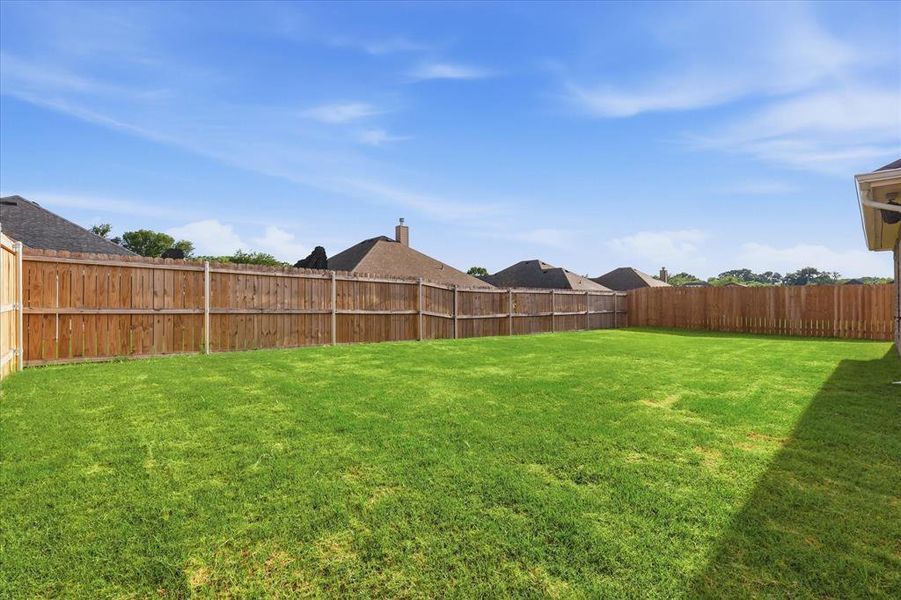 Fenced grassy backyard offering plenty of space for outdoor activities, pets, and entertaining.