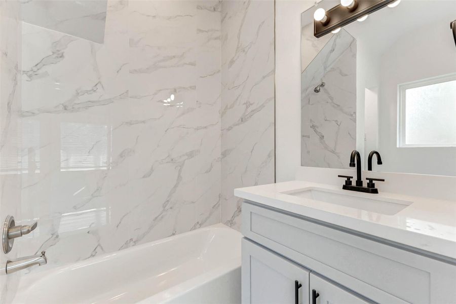 Contemporary elegance shines in this full bath, complete with a quartz-topped vanity, bold matte black fixtures, and full-height marble-style tile that elevates everyday routines. Contemporary elegance shines in this full bath, complete with a quartz-topped vanity, bold matte black fixtures, and full-height marble-style tile that elevates everyday routines.