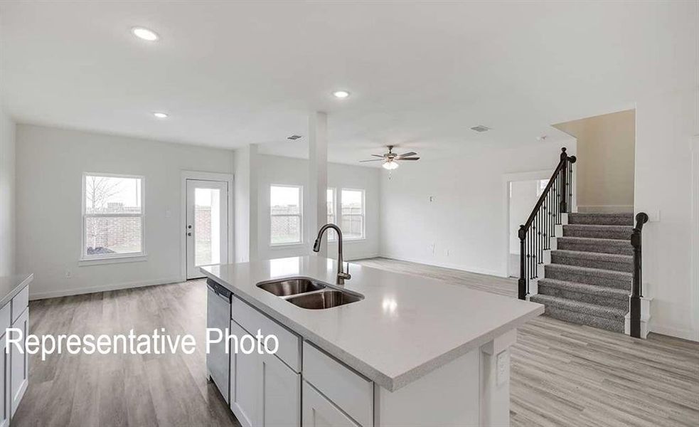 Kitchen with light wood-type flooring, stainless steel dishwasher, an island with sink, and sink