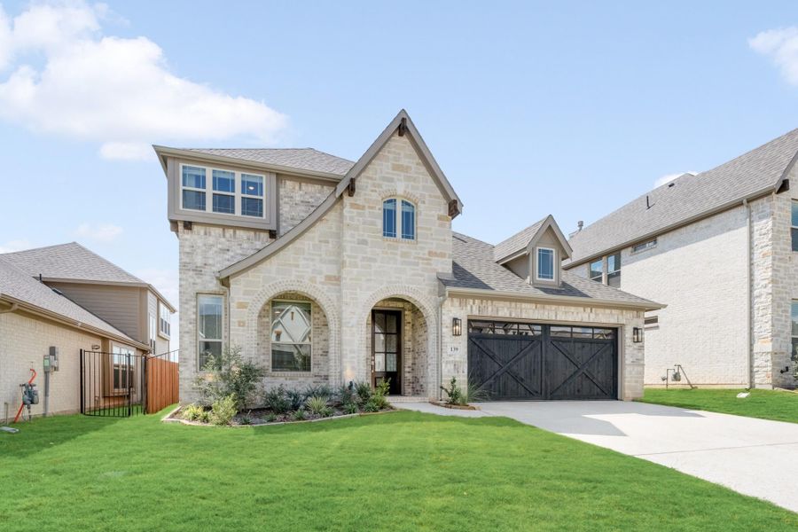 Two-story stone home with arched entry, dark wood garage door, and manicured front lawn