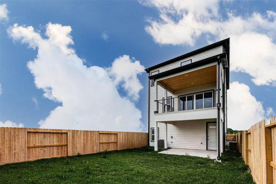 An angled backyard perspective showcases both the depth of the lot and the elevated outdoor living features. The covered patio offers shade and comfort, while the upper balcony adds versatility for relaxing or entertaining. Surrounded by a private fence and open sky, this outdoor space delivers both function and tranquility. The picture shown is from the model home with the same floor plan, Rev floor plan.