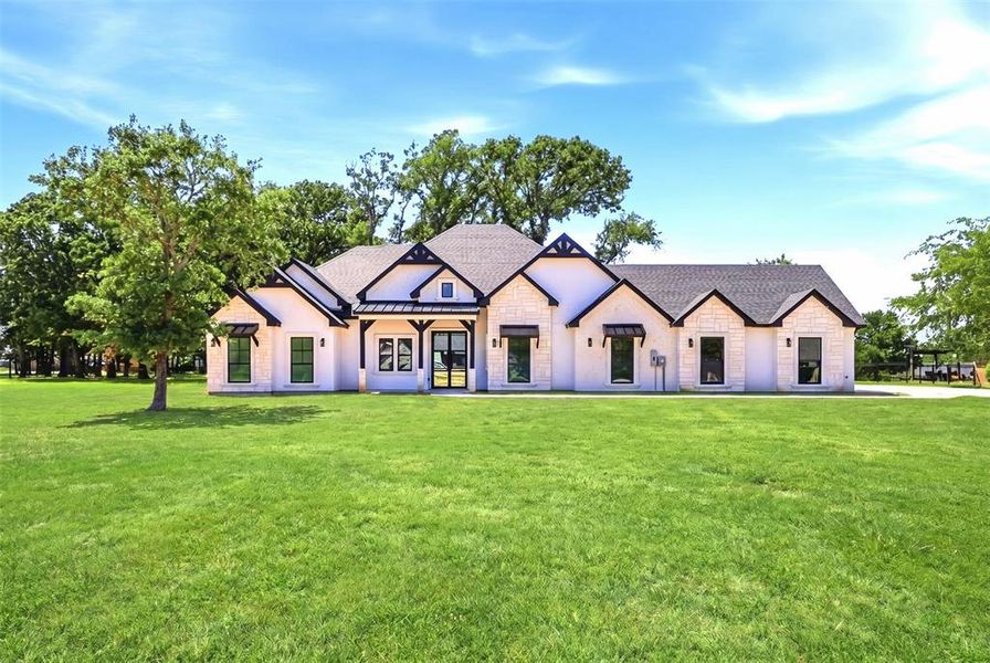 Modern ranch-style home featuring a stone and stucco exterior, dark shingle roof, black window frames, and decorative wood accents