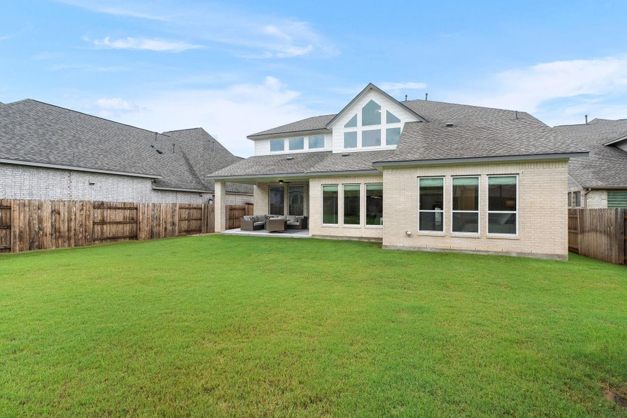 A pristine lawn stretches towards a modern residence with an inviting covered patio, ideal for outdoor leisure.
