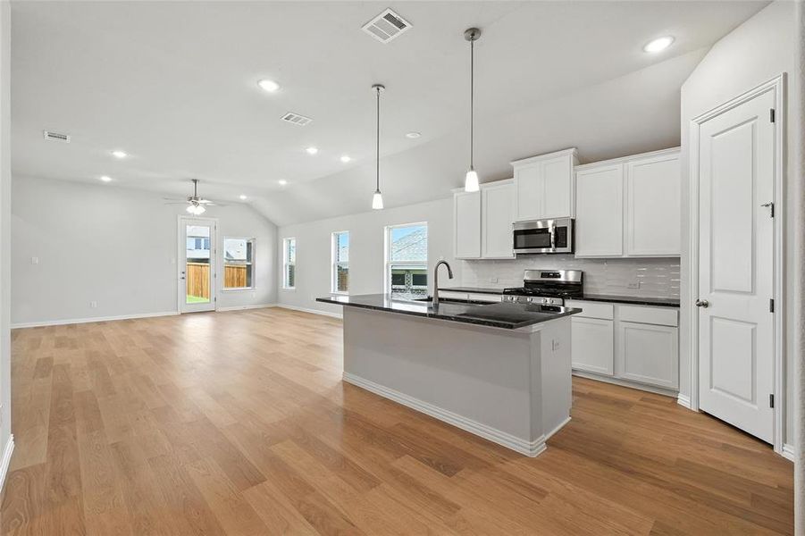 Kitchen with vaulted ceiling, an island with sink, white cabinets, stainless steel appliances, and tasteful backsplash