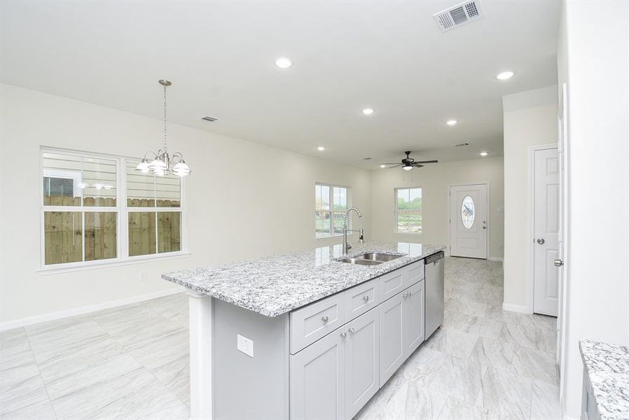 New, empty kitchen with gray cabinets, marble countertops, tiled floor, and a chandelier over dining area. Large window overlooks a wooden fence.