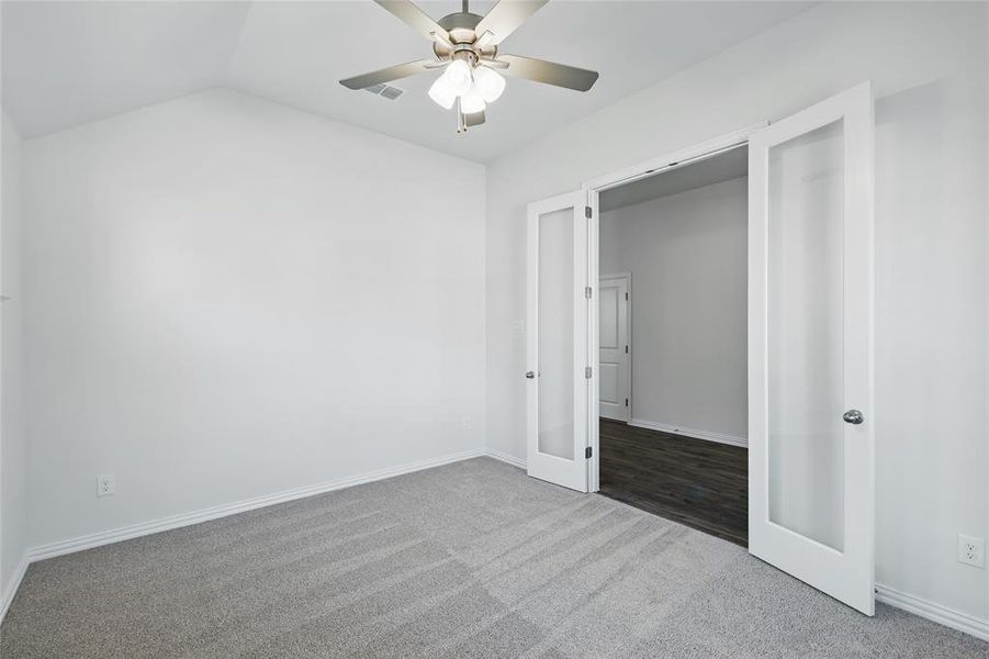 Unfurnished bedroom with vaulted ceiling, carpet floors, visible vents, and baseboards